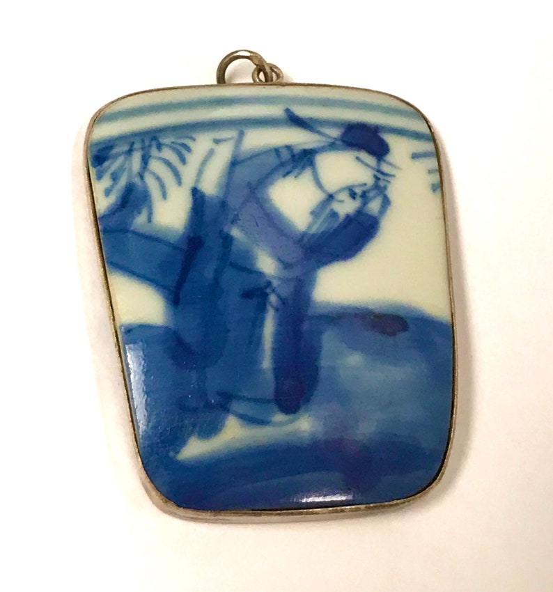 May include: A blue and white porcelain pendant with a silver frame. The pendant features a hand-painted design of a person in traditional Chinese clothing.