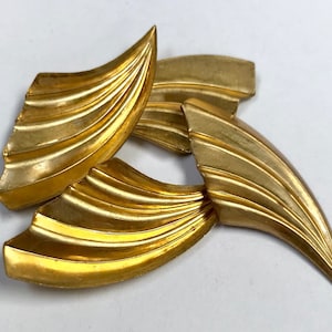 May include: Three gold-coloured metal pieces shaped like stylised leaves with a ridged texture.