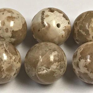 May include: Six round beads with a marbled appearance. The beads are primarily beige with patches of off-white and brown. Some beads have small holes. These beads could be used for jewelry making or other crafts.