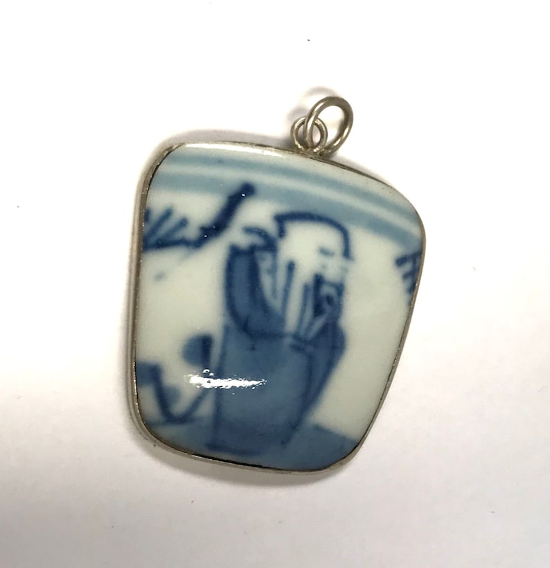 May include: A silver pendant with a blue and white porcelain inset featuring a Chinese figure in a landscape scene.
