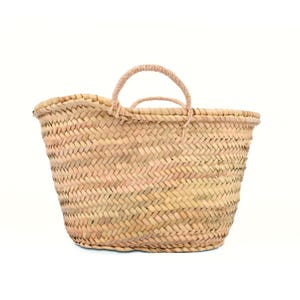 May include: A woven straw tote bag with two handles. The bag is made of natural-colored straw and has a basket-like weave. The handles are a lighter shade of straw and are looped. The bag is empty and sits against a white background.