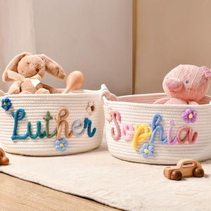 Puede incluir: Dos cestas de almacenamiento redondas de cuerda trenzada color blanco roto con nombres personalizados en letras de lana de colores. Una cesta muestra el nombre Luther en azul y marr&oacute;n, y la otra Sophia en rosa, amarillo y azul, decoradas con flores de lana.