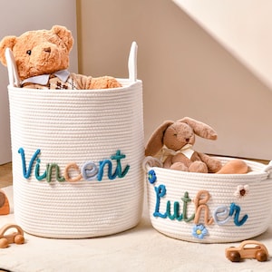 Puede incluir: Dos cestas cil&iacute;ndricas de cuerda blanca con asas integradas. La cesta m&aacute;s alta lleva el nombre Vincent en hilo azul, verde y beige. La cesta m&aacute;s baja lleva el nombre Luther en los mismos colores, decorada con peque&ntilde;as flores azules y blancas.