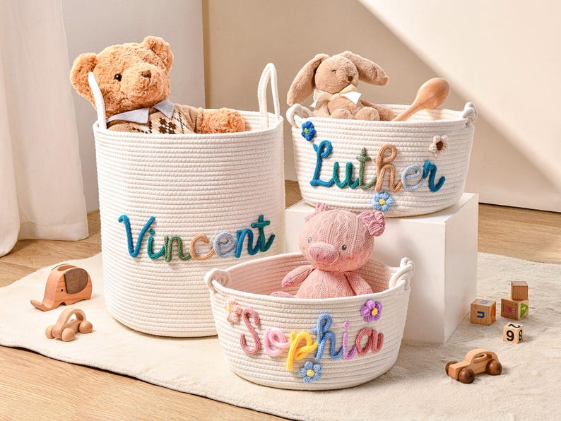 Puede incluir: Tres cestas de almacenamiento de cuerda de algod&oacute;n tejida blanca con asas. Las cestas presentan nombres bordados de colores: Vincent, Luther y Sophia. Cada cesta est&aacute; decorada con peque&ntilde;as flores de tela y contiene un peluche: un oso, un conejo y un cerdo.
