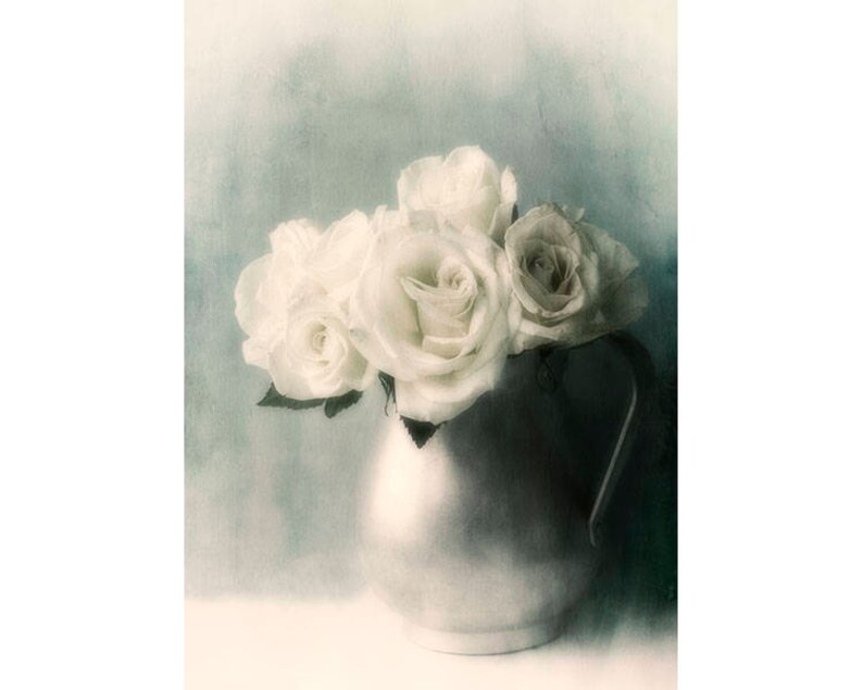 May include: A bouquet of white roses in a silver pitcher against a blue-green background.