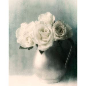 May include: A bouquet of white roses in a vintage, silver pitcher. The roses are arranged in a soft, romantic style, with their petals gently overlapping. The background is a soft, muted blue.
