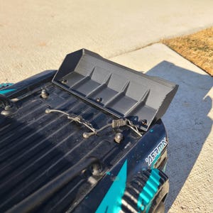Peut inclure: Un camion télécommandé noir et turquoise avec un aileron arrière en plastique noir. Le camion porte l'inscription "ARRMA" sur le côté.