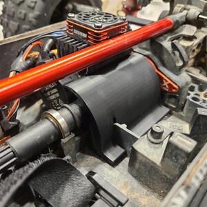 Puede incluir: Primer plano de un motor eléctrico negro y rojo con un ventilador de refrigeración y una varilla de metal roja unida a él. El motor está montado en un chasis negro con un engranaje negro y plateado.