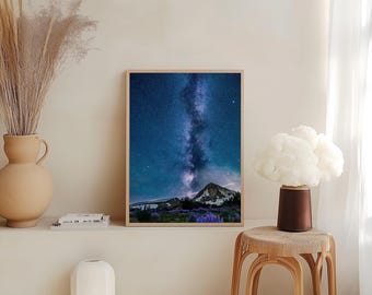 May include: A framed print featuring a night sky with the Milky Way over a mountain range. The image has a wooden frame and is displayed on a shelf with decorative items, including a vase with dried plants and a white, ribbed vase.
