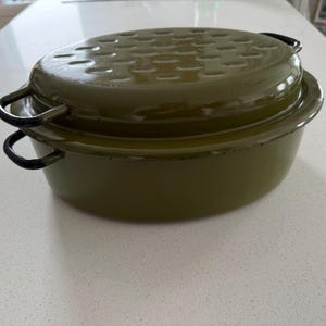 Könnte beinhalten: Olivgrüne ovale Bratpfanne mit passendem Deckel. Der Deckel hat eine Reihe kleiner Löcher. Die Pfanne hat zwei schwarze Griffe. Ein Küchenartikel.
