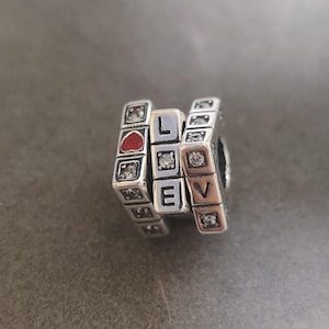 May include: Silver charm with a red heart and the word "LOVE" spelled out in individual silver blocks with clear crystals.