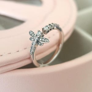 May include: A silver ring with a dragonfly design featuring clear cubic zirconia stones.