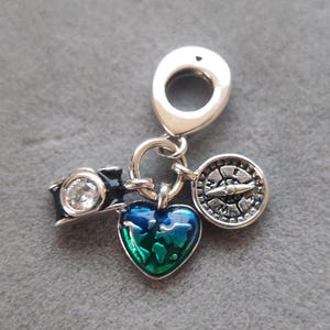 May include: Silver charm with a black camera, a compass, and a heart with a green and blue globe design.