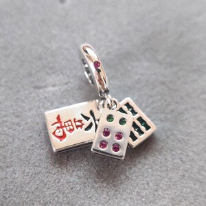 Puede incluir: Un charm de plata con tres colgantes rectangulares. Un colgante tiene texto rojo y los otros dos tienen gemas de colores. El charm est&aacute; dise&ntilde;ado para sujetarse a una pulsera o collar. Un accesorio con tem&aacute;tica de juego.