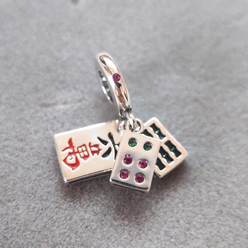 Puede incluir: Un charm de plata con tres colgantes rectangulares. Un colgante tiene texto rojo y los otros dos tienen gemas de colores. El charm est&aacute; dise&ntilde;ado para sujetarse a una pulsera o collar. Un accesorio con tem&aacute;tica de juego.