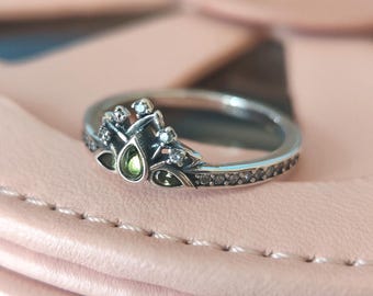 May include: A silver ring with a green stone and clear stones set in a crown design.