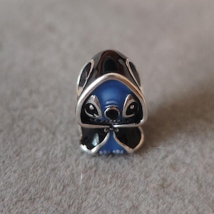 May include: A silver charm featuring a blue and black character design. The charm has a detailed face with large eyes and a small nose. The character's head is blue, and the charm has a shiny silver finish.