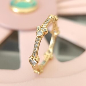 Puede incluir: Un anillo de oro con una fila de piedras de circonita c&uacute;bica transparentes y un dise&ntilde;o de cabeza de Mickey Mouse con una piedra de circonita c&uacute;bica transparente m&aacute;s grande en el centro.