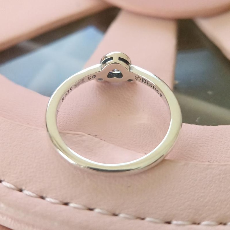 May include: A silver ring with a heart-shaped charm and the inscription "Disney" on the band.