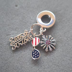 Puede incluir: Encanto de plata con un globo rojo, blanco y azul, gafas de sol y un fuego artificial. El encanto también tiene las palabras "Stars & Stripes" en él.