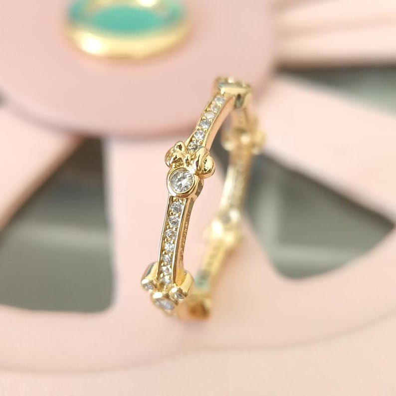 Puede incluir: Un anillo de oro con una fila de peque&ntilde;as piedras transparentes y un dise&ntilde;o de cabeza de Mickey Mouse con una piedra transparente en el centro.