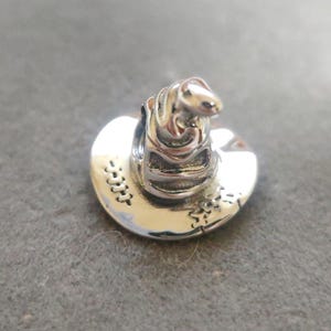 Op de afbeelding: Een zilveren bedel in de vorm van een honkbalpet. De bedel heeft gedetailleerde stiksels en een gebogen klep. De bovenkant van de pet heeft een klein, afgerond ontwerp. De bedel is gemaakt van glanzend, reflecterend metaal.