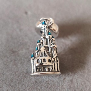 May include: Silver charm in the shape of a castle with blue accents. The charm has a loop at the top for attaching to a bracelet or necklace.