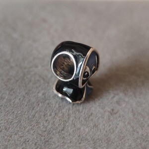 May include: A black and silver charm with a panda bear design. The charm has a glossy black finish with silver accents and a detailed panda face. The charm is likely made of metal and is designed to be used with a bracelet or necklace.