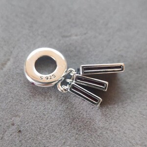 Puede incluir: Un charm de plata con tres colgantes rectangulares con esmalte rojo oscuro. El charm tiene un lazo circular con la marca "S 925". Este charm est&aacute; dise&ntilde;ado para ser usado con una pulsera o collar.