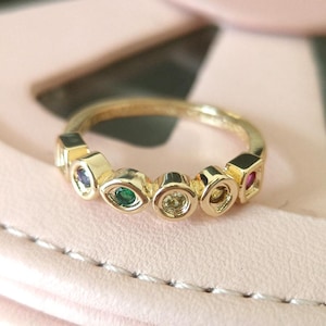 May include: Gold ring with a row of colorful gemstones. The gemstones are set in different shapes, including squares, ovals, and teardrops.