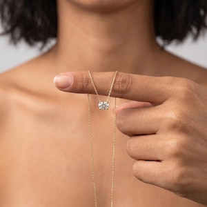 May include: A delicate gold chain necklace featuring a single round, brilliant-cut clear gemstone pendant held in a four-prong setting. The thin, polished gold chain suspends the sparkling stone, which rests against the skin, showcasing a classic design.