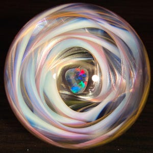 May include: A glass orb with a swirling pattern of white, pink, and blue. A small iridescent opal is visible in the center of the orb.