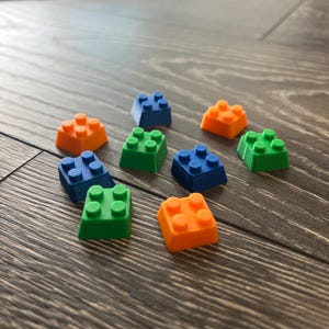 May include: Nine small plastic building blocks in blue, green, and orange. The blocks are arranged in a loose pattern on a wood surface.