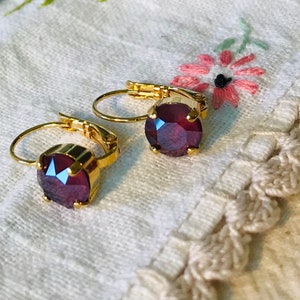 Könnte beinhalten: Ein Paar goldene Creolen mit einem tiefvioletten Edelstein in der Mitte jedes Creolen.