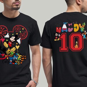 May include: Black t-shirt with a vibrant Disney-themed design. The front features Mickey Mouse and friends, with the text "Disney Trip 2-26". The back displays "Daddy 10" with Disney characters. A fun, themed apparel item.