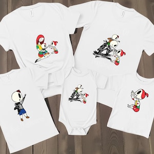 May include: White t-shirts and a onesie featuring cartoon characters in various poses. The designs include a skeleton character and other figures in colorful outfits. The shirts are likely for a family or group.