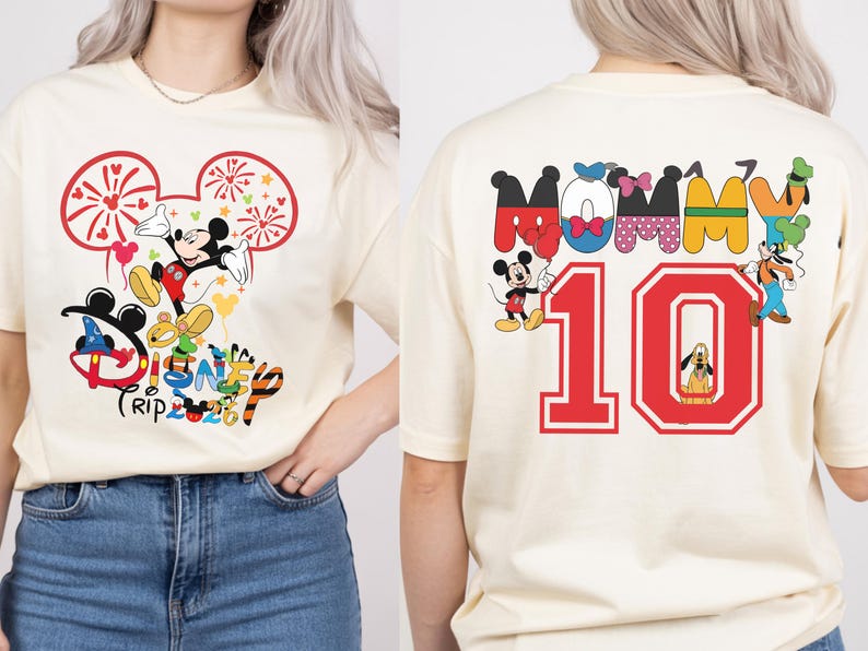 May include: Cream-coloured t-shirt with a Mickey Mouse graphic and the text "Disney Trip 2023" on the front. The back of the shirt shows the word "Mommy" and the number "10" with Disney character graphics. A fun, colourful design.