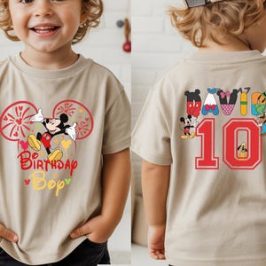 May include: Tan short-sleeve t-shirt featuring Mickey Mouse with the text "Birthday Bop" on the front. The back of the shirt has the number "10" in red, along with various Disney character designs.