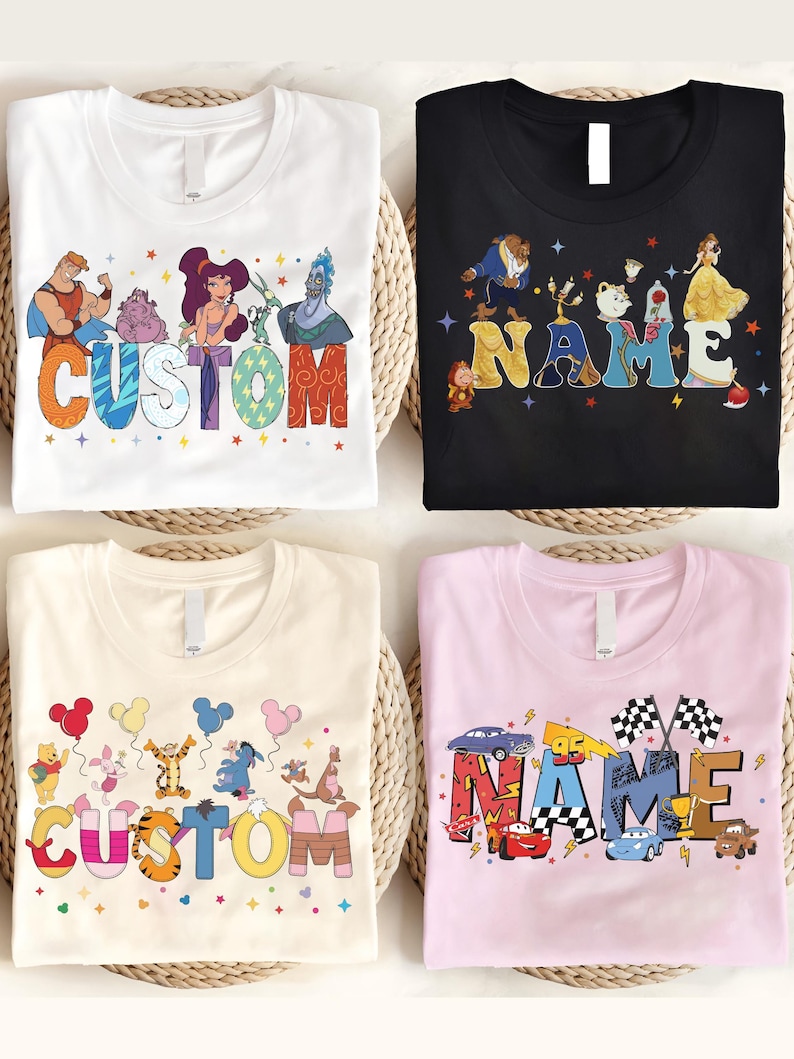 K&ouml;nnte beinhalten: Vier T-Shirts mit Zeichentrickfiguren-Designs. Ein wei&szlig;es Shirt hat das Wort "CUSTOM" mit Figuren aus Hercules. Ein schwarzes Shirt hat das Wort "NAME" mit Figuren aus Die Sch&ouml;ne und das Biest. Ein beiges Shirt hat "CUSTOM" mit Winnie-Puuh-Figuren. Ein rosa Shirt hat "NAME" mit Rennwagen-Figuren.