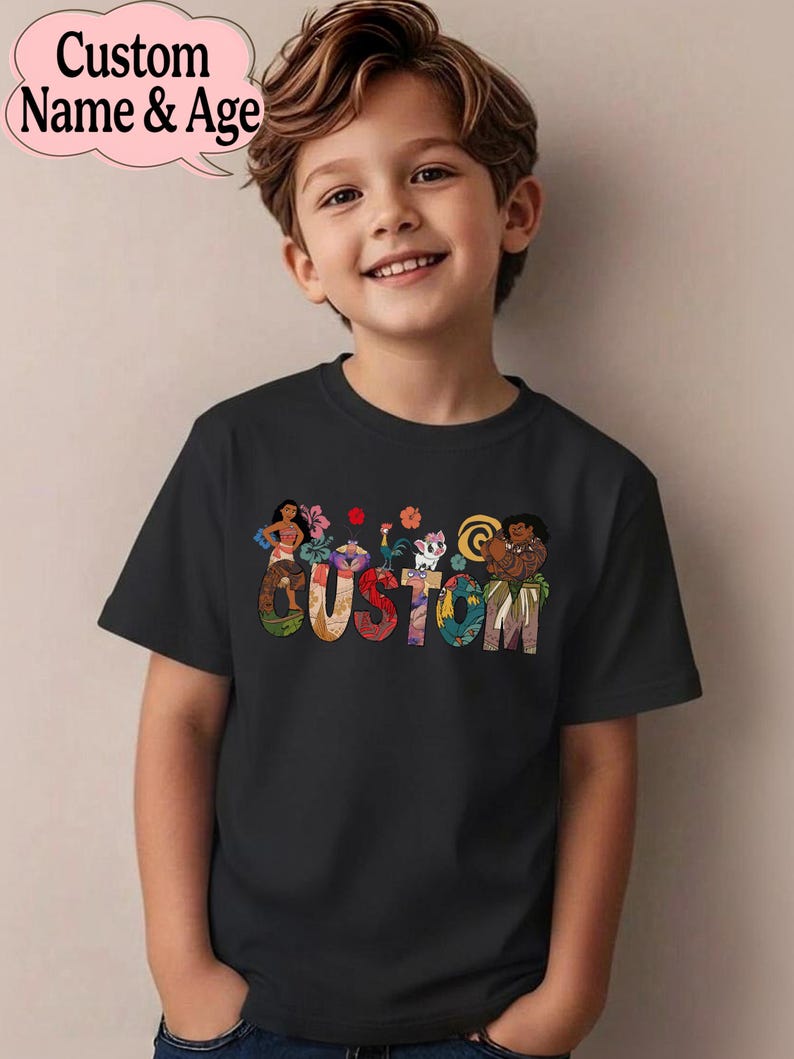 May include: Black t-shirt featuring the word "CUSTOM" in colorful, patterned letters. Above the word are cartoon characters and flowers. The shirt is worn by a smiling child. A pink speech bubble with the text "Custom Name & Age" is in the upper left corner.