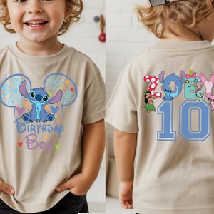 May include: Tan short-sleeved t-shirt featuring a blue cartoon character design with the text "Birthday Boy" on the front. The back of the shirt displays the name "Zoey" and the number "10" in blue.