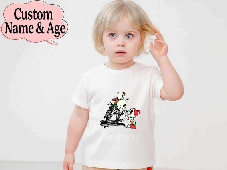 May include: White t-shirt featuring a cartoon graphic of Jack Skellington and other characters from The Nightmare Before Christmas. The word "nightmares" is printed below the graphic. A pink speech bubble with the text "Custom Name & Age" is in the top left corner.