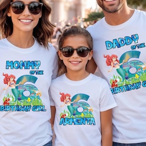 May include: White t-shirts with a mermaid theme. Each shirt has a different text: "Mommy of the Birthday Girl", "Daddy of the Birthday Girl", and a personalized name. The number "6" is featured prominently.