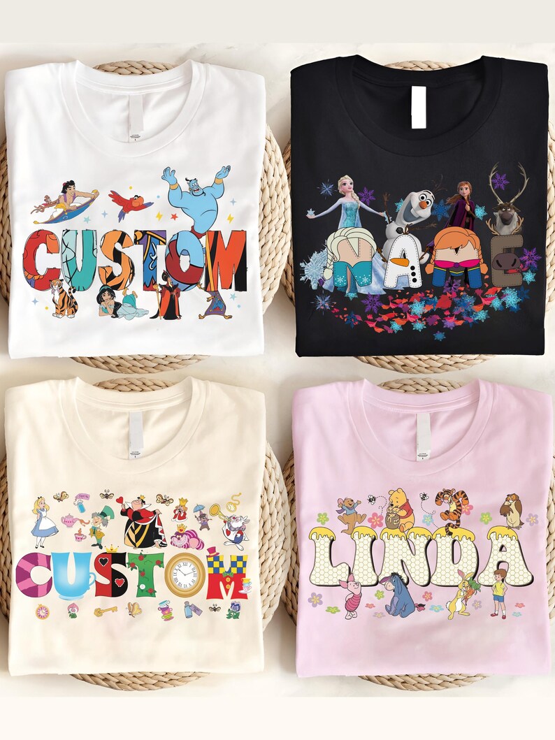 K&ouml;nnte beinhalten: Vier T-Shirts mit Zeichentrickfiguren-Designs. Ein wei&szlig;es T-Shirt mit "CUSTOM" in bunten Buchstaben und Aladdin-Figuren. Ein schwarzes T-Shirt mit "NAME" und Frozen-Figuren. Ein cremefarbenes T-Shirt mit "CUSTOM" und Alice im Wunderland-Figuren. Ein rosa T-Shirt mit "LINDA" und Winnie-the-Pooh-Figuren.