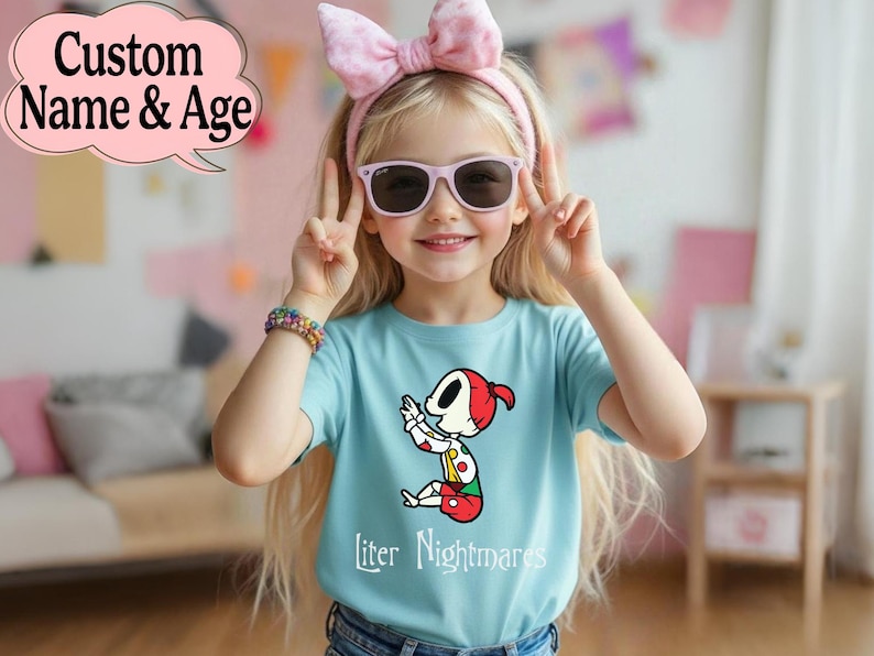 May include: A young girl wearing a light blue t-shirt with a cartoon character design and the text "liter Nightmares". She is wearing a pink bow headband, sunglasses, and a colorful bracelet. The image also includes the text "Custom Name & Age".