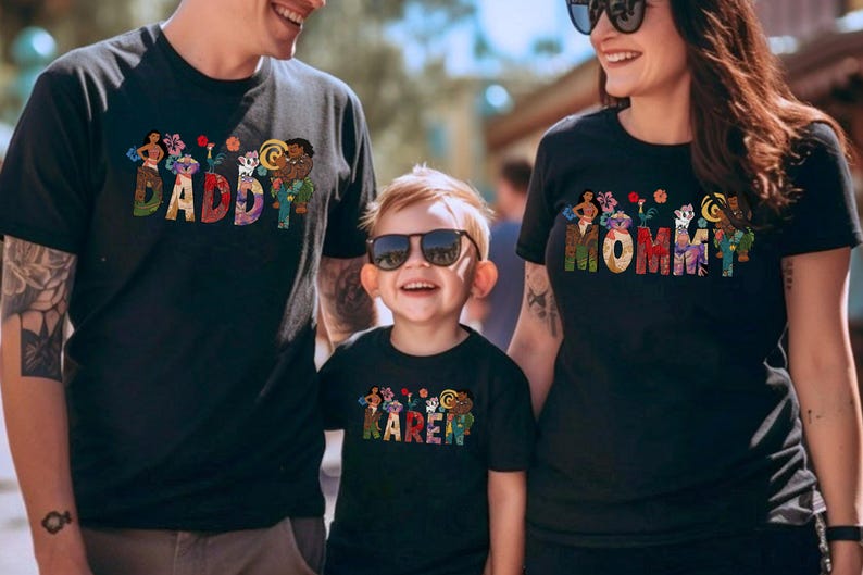 May include: Black t-shirts with colorful text and graphics. The shirts say "DADDY", "MOMMY", and "KAREN" in a decorative font with floral and character designs. The family is smiling and wearing sunglasses.
