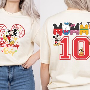 May include: Cream-colored t-shirt featuring Mickey Mouse with fireworks and the text "Birthday Bop" in red and yellow. The back of the shirt displays the word "Mommy" and the number "10" with Disney characters.
