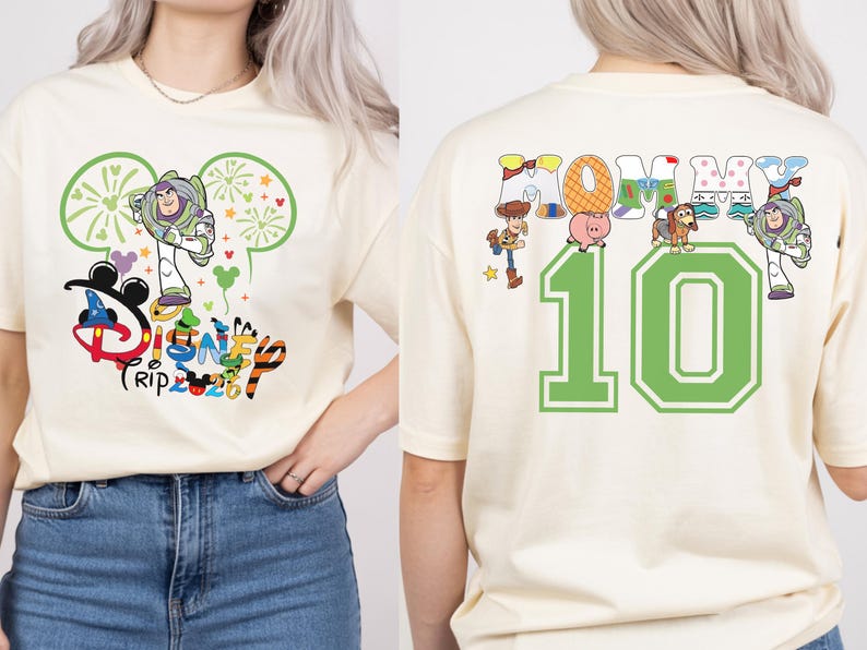 May include: Cream-coloured t-shirt with a Disney Trip 2023 graphic featuring Buzz Lightyear. The back of the shirt shows the word "Mommy" with Toy Story characters and the number "10" in green.