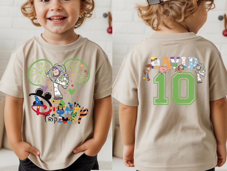 May include: A tan short-sleeved t-shirt with a colourful Disney Trip graphic featuring Buzz Lightyear and Mickey Mouse ears. The back of the shirt shows the name "DAVID" above the number "10" with Toy Story characters.