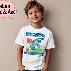 May include: White t-shirt with the text "BROTHER OF THE 6 BIRTHDAY GIRL" in blue. The shirt features a mermaid graphic. A pink speech bubble with the text "Custom Name & Age" is in the upper left corner. The shirt is worn by a young boy.